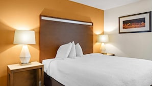 Ett hotellrum med en stor säng, två sänglampor, en inramad tavla på väggen och en sänggavel i trä.