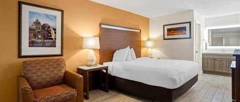 Una habitación de hotel con una cama, dos lámparas de noche, una silla y dos cuadros en las paredes.
