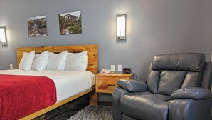 Ein Hotelzimmer mit einem Bett mit Holz-Kopfteil, einer roten Decke, einem grauen Ledersessel und zwei Wandleuchten.