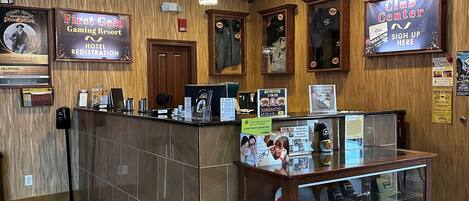 A hotel reception area with a wooden interior, a chandelier, a sign-up board, and a display case with hats.