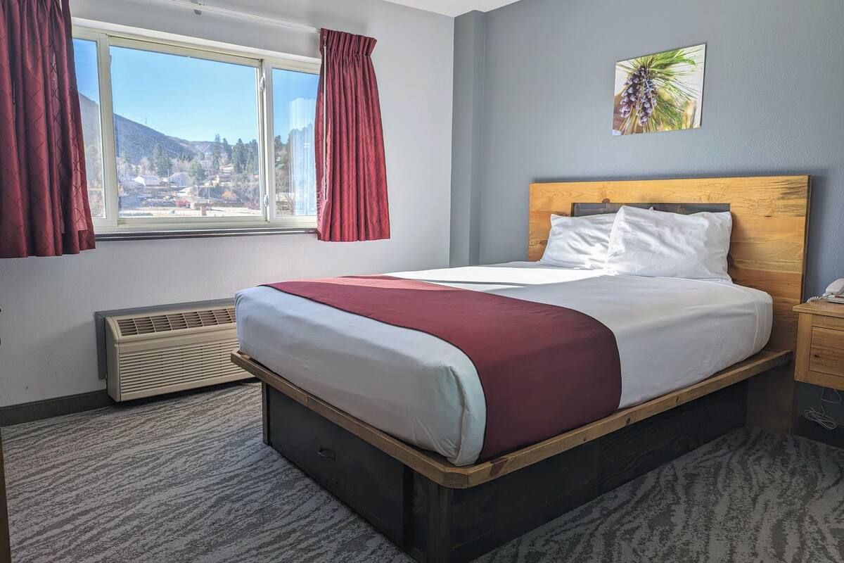 Une chambre d’hôtel avec un grand lit, une fenêtre avec des rideaux, un climatiseur fixé au mur et une petite table de chevet.