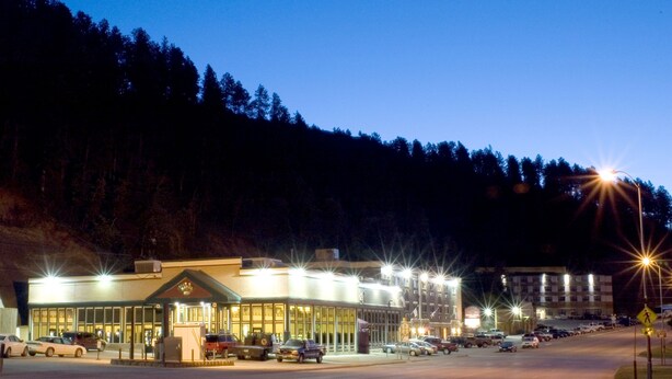 Ein Hotel mit großem Parkplatz, ein mehrstöckiges Gebäude und ein bewaldeter Hügel im Hintergrund.