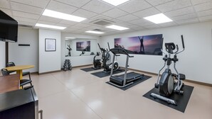 Ein Fitnessraum mit Trainingsgeräten, einem Fernseher und einem Tisch.