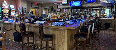 Un bar con varias pantallas, una caja registradora y taburetes.