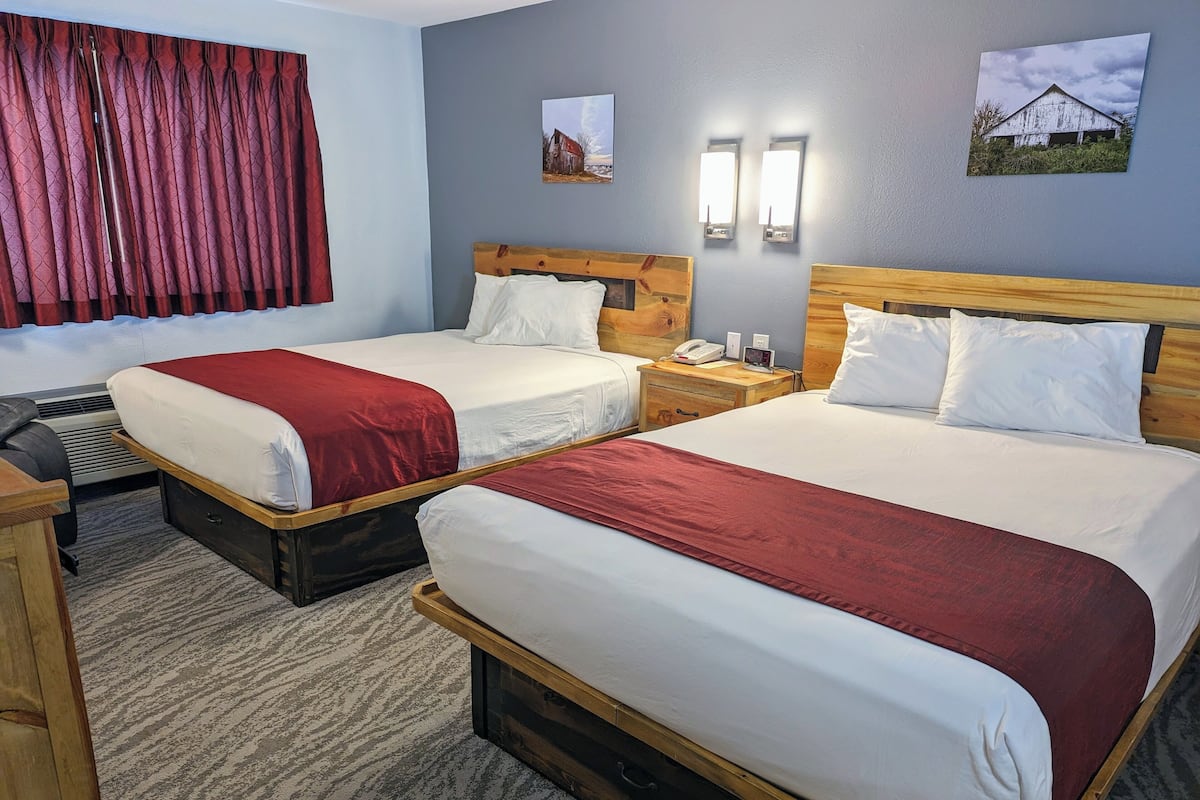 Une chambre d’hôtel avec deux lits, une tête de lit en bois, une table de chevet avec un téléphone et une fenêtre avec des rideaux rouges.