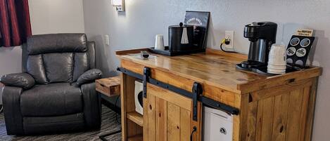 A compact living space with a leather recliner, a small wooden bar with a coffee maker, and a television mounted on the wall.