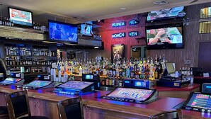 Eine Bar mit mehreren Spirituosenflaschen, einer Registrierkasse und Barhocker.