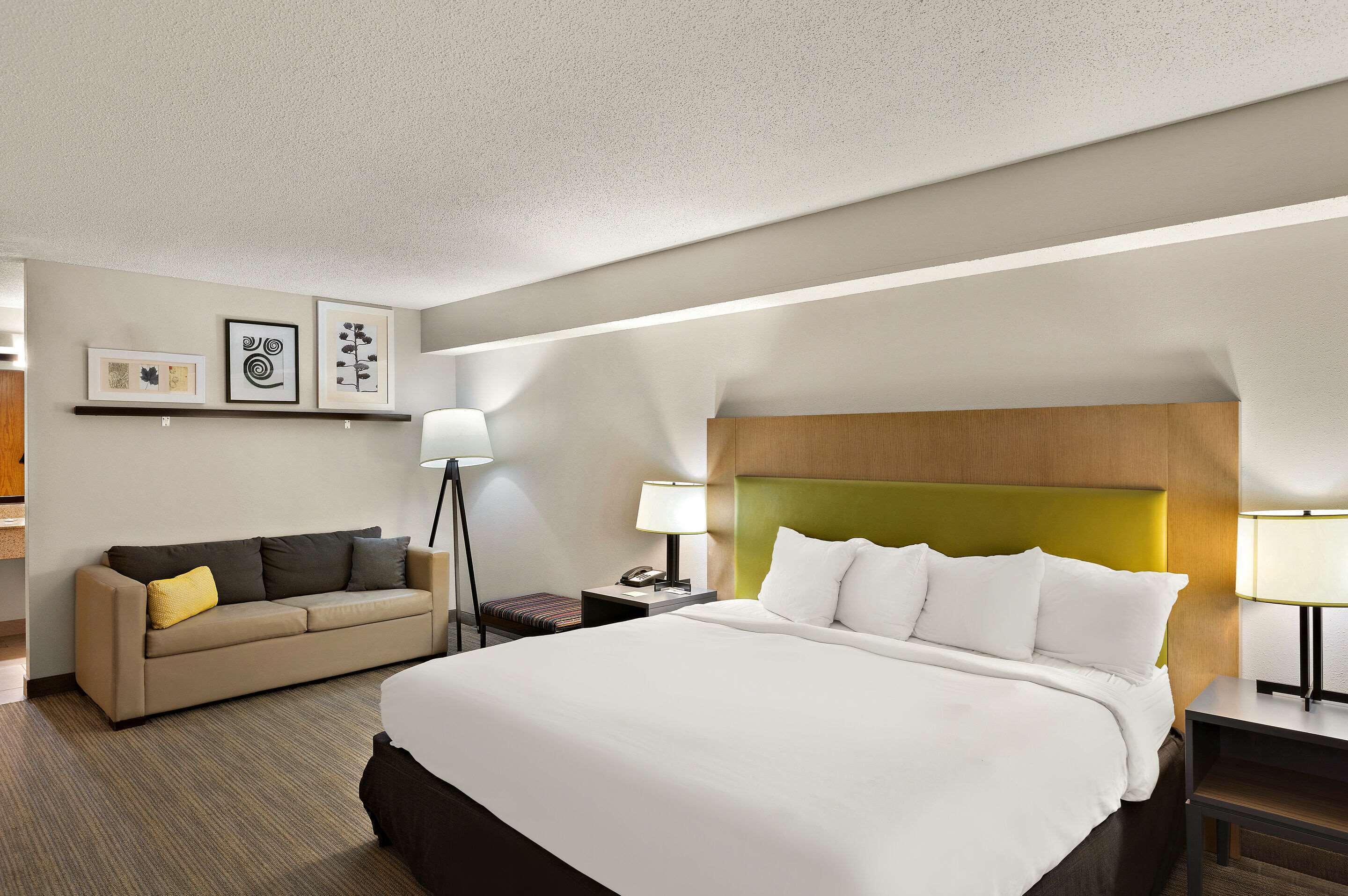 Une chambre d’hôtel avec un grand lit, un canapé, une table de chevet avec une lampe et des œuvres d’art encadrées accrochées au mur.