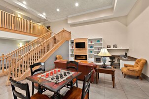 A spacious living area with a wooden staircase, a dining table with a board game, and a cozy seating area with a lamp.