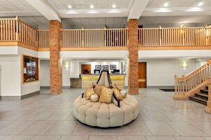 Um hall amplo com área de estar central, balcão de recepção e escadaria.