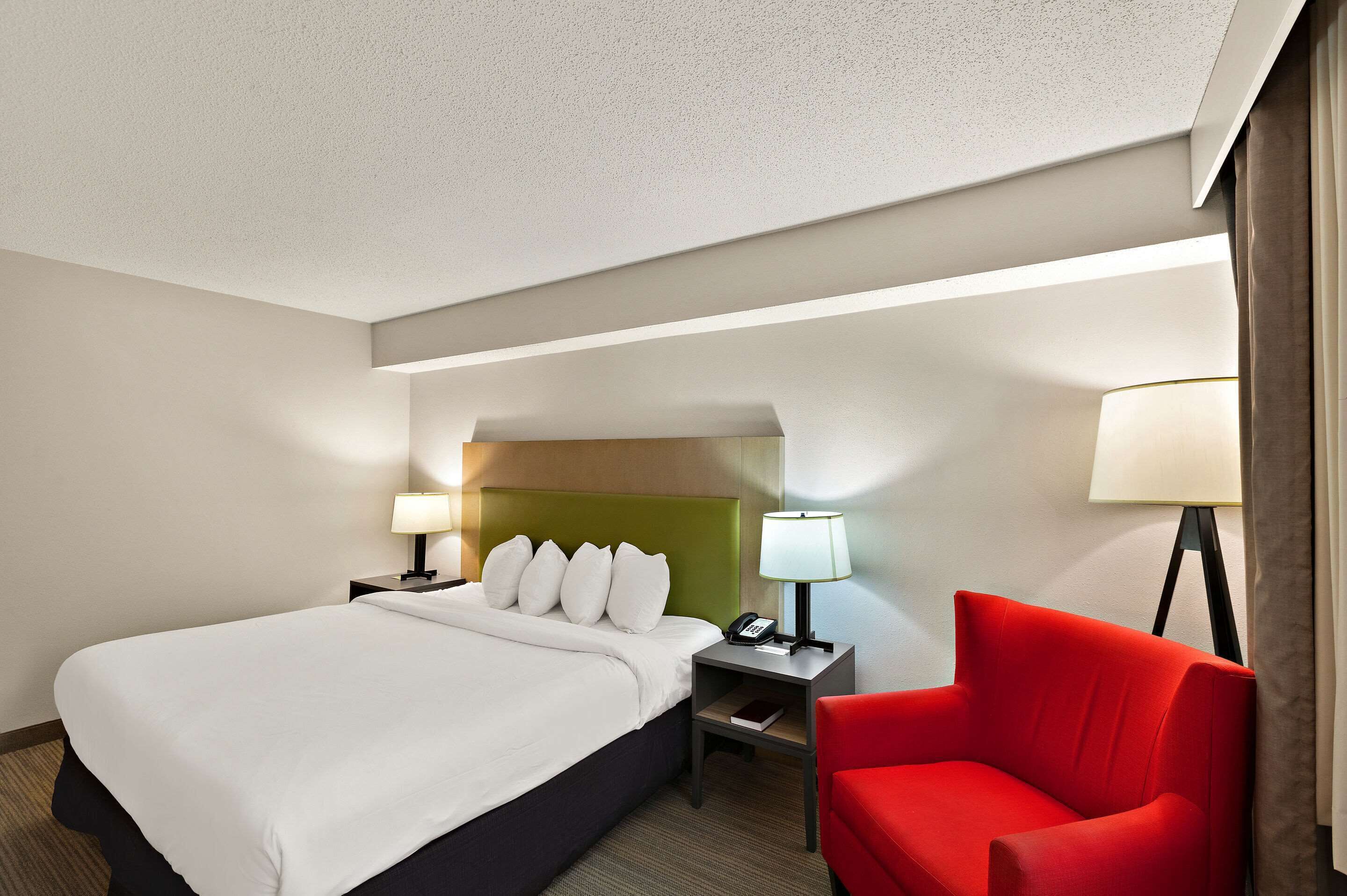 A hotel room with a large bed, a green headboard, two bedside tables with lamps, and a red armchair.