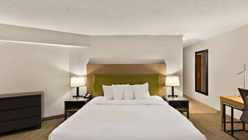 A hotel room with a large bed, two bedside tables with lamps, a desk, and a chair.