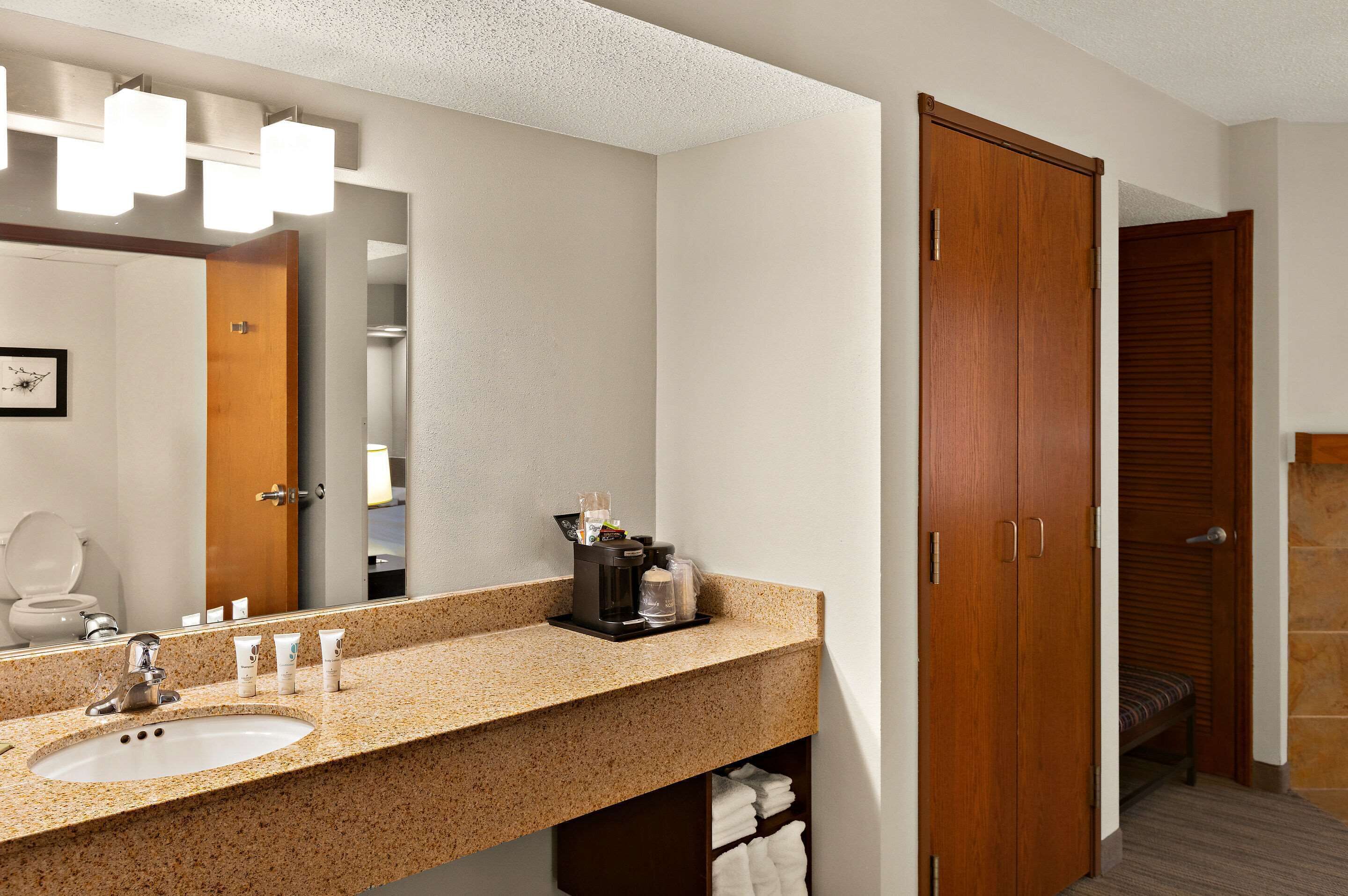 Baño con lavamanos de encimera de granito, espejo y puerta de madera.