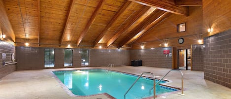 An indoor swimming pool with wooden beams, a clock, and a tiled wall.