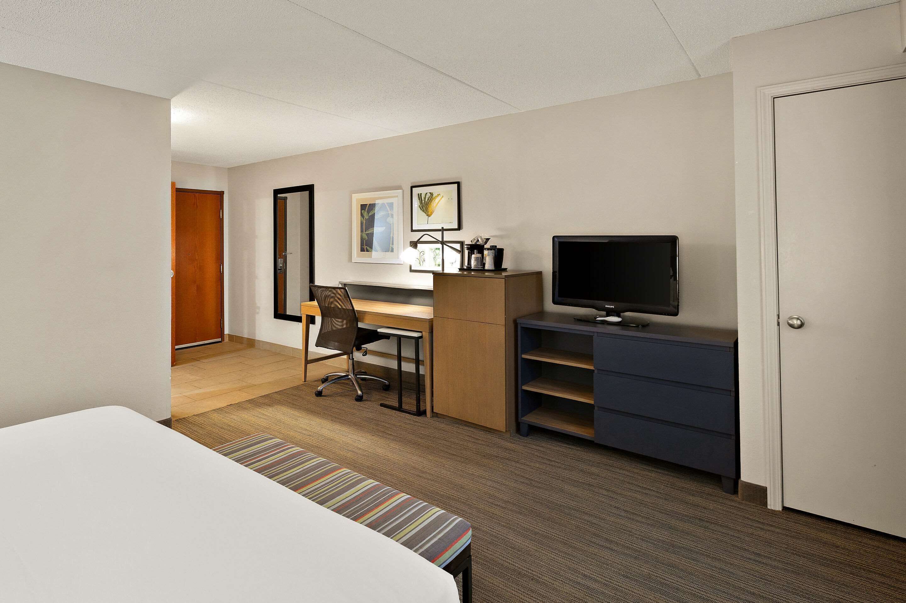 A hotel room with a bed, a desk with a chair, a television, and a wardrobe.