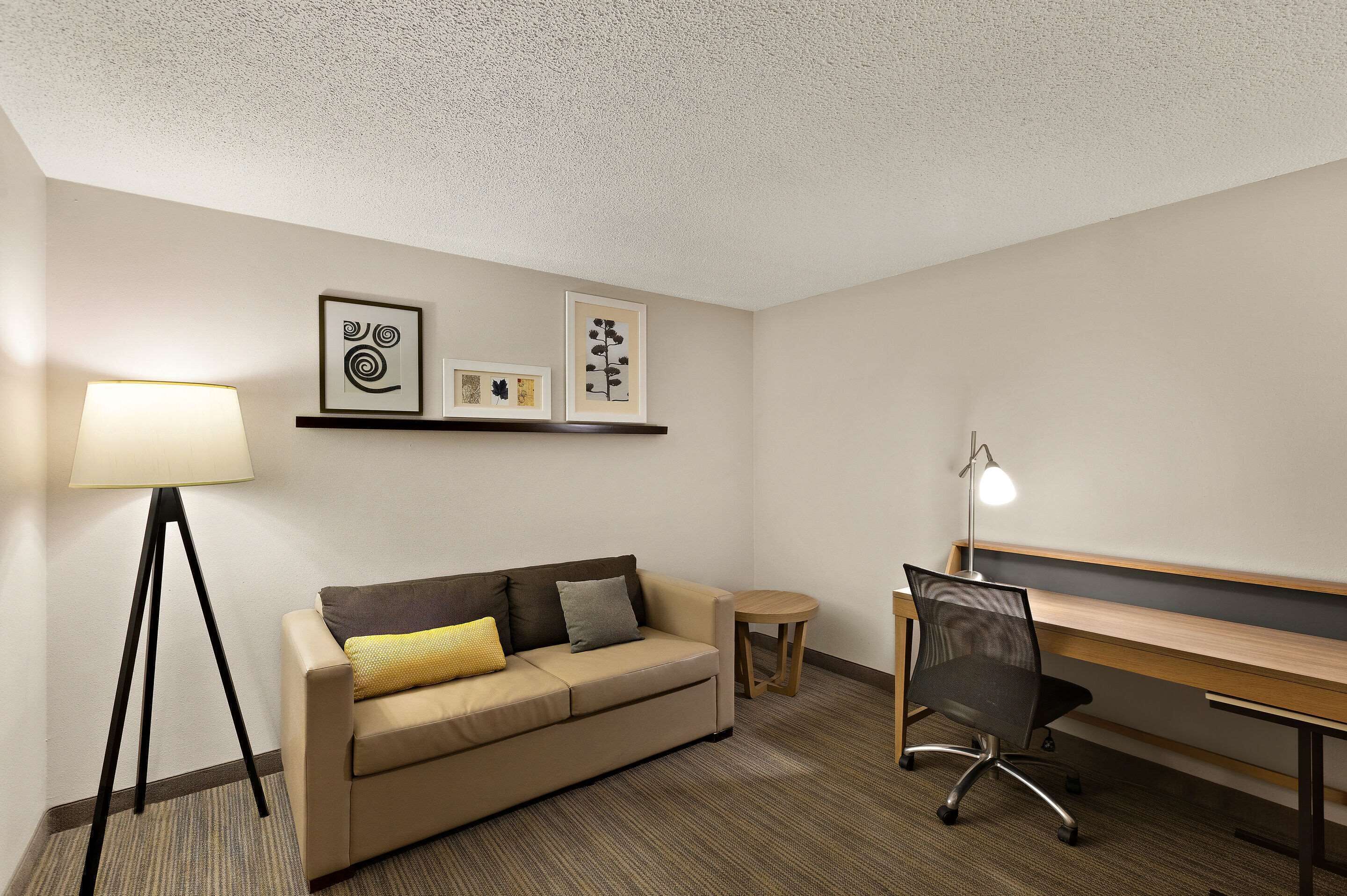 Une chambre d’hôtel avec un canapé, un bureau, une lampe et des œuvres d’art encadrées accrochées au mur.