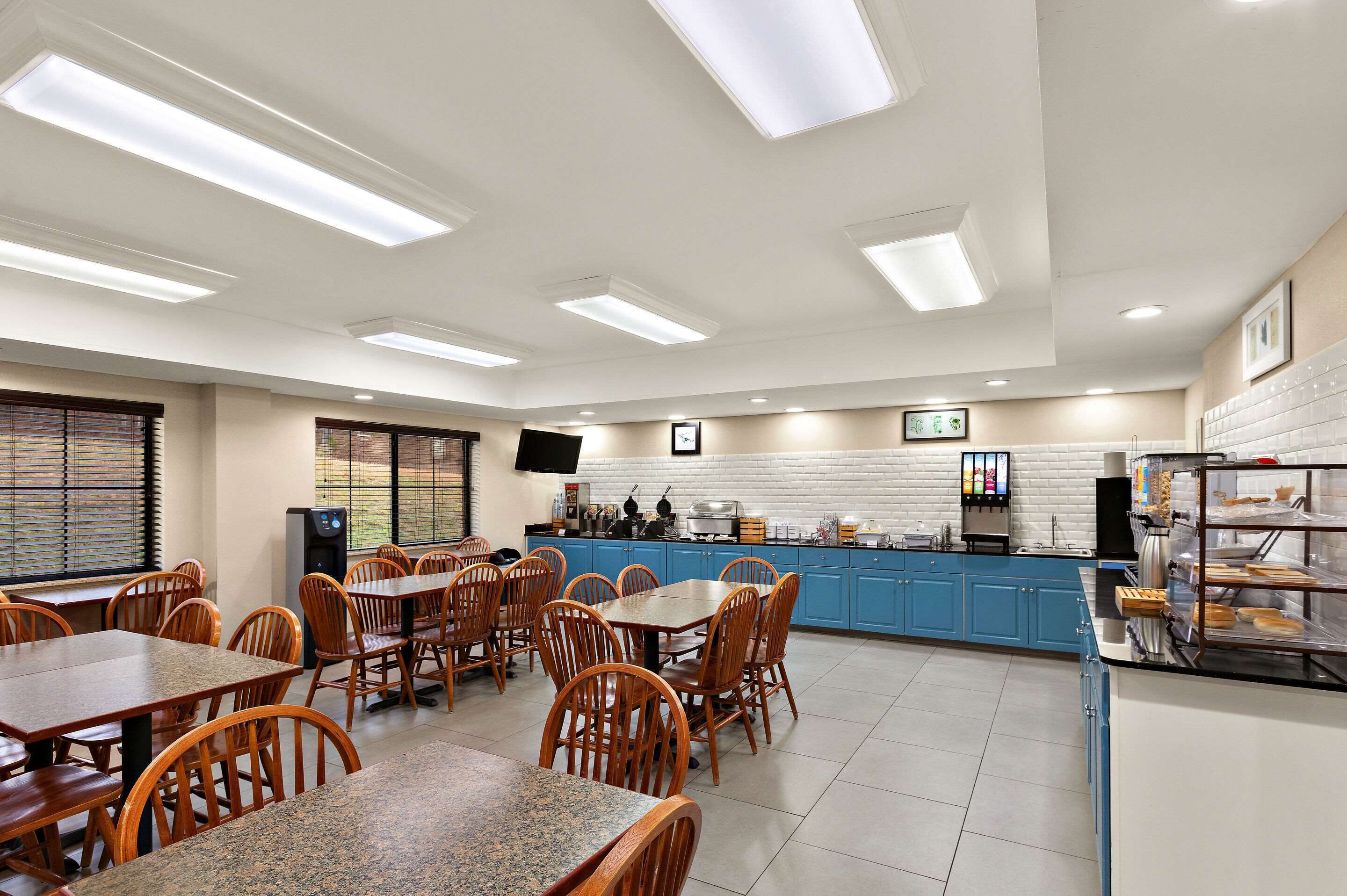 A spacious dining area with multiple tables and chairs, a kitchen counter with various appliances, and a television mounted on the wall.