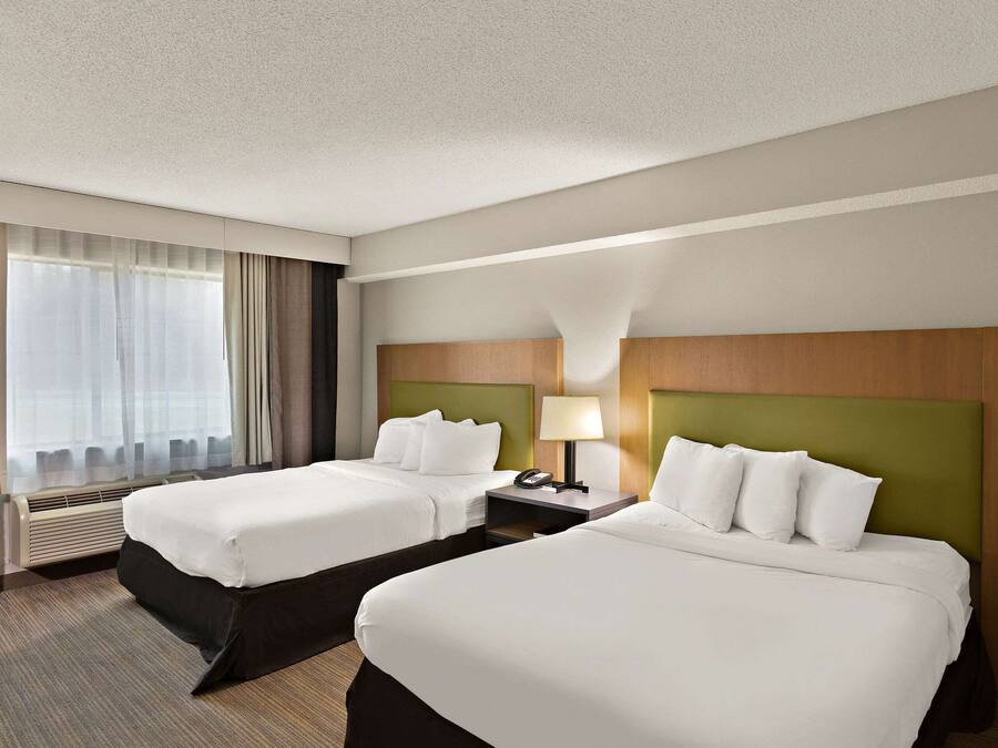 A hotel room with two beds, a nightstand with a lamp, and a large window with curtains.