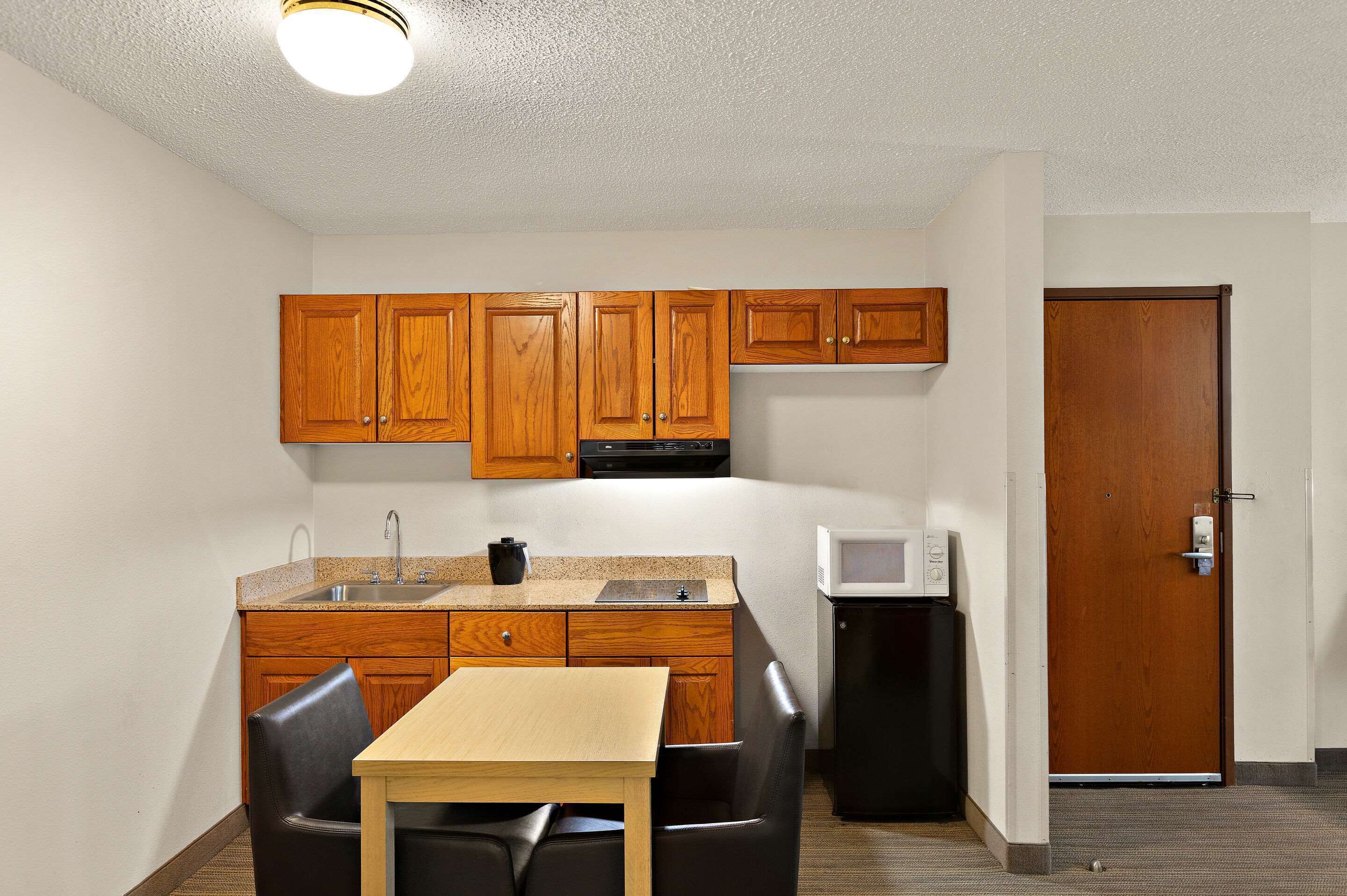 A compact kitchen with wooden cabinets, a microwave, and a small refrigerator.