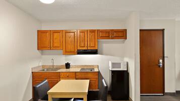 A compact kitchen with wooden cabinets, a microwave, and a small refrigerator.