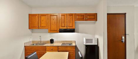 A compact kitchen with wooden cabinets, a microwave, and a small refrigerator.
