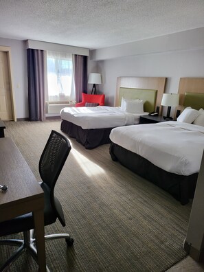 A hotel room with two beds, a desk, a chair, and a window with curtains.