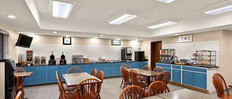 A restaurant with blue cabinets, wooden chairs, granite tables, and a flat-screen TV mounted on the wall.