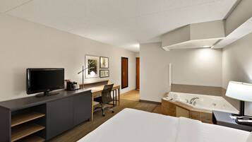 A hotel room with a bed, a desk with a TV, a chair, a bathroom with a bathtub, and a lamp.