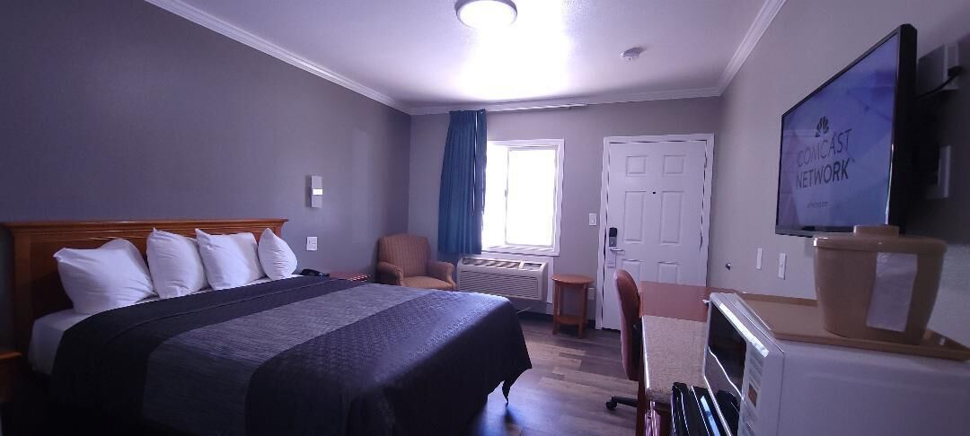 Een hotelkamer met een bed, een bureau, een stoel, een televisie en een raam met gordijnen.