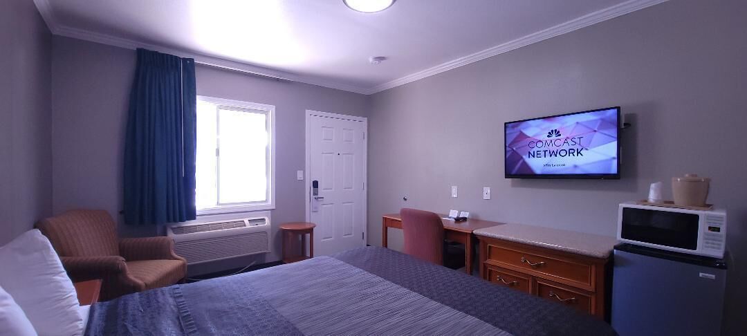 Una habitación de hotel con cama, escritorio, silla, televisor y microondas.