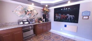 A hotel reception area with a counter, coffee station, and a painting of horses.