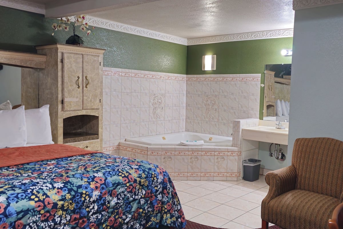 Habitación de hotel con una cama, una silla, un baño con bañera y lavamanos.
