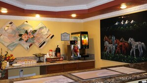 Un espace d’accueil d’hôtel équipé d’une machine à café, d’un distributeur de jus de fruits et d’une pancarte indiquant que le petit-déjeuner est offert.