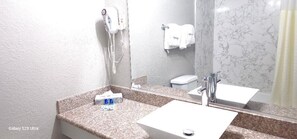 A bathroom with a granite countertop, a white sink, a mirror, a hairdryer, and a towel rack.