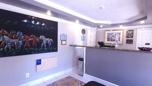 Un espace d’accueil agrémenté d’une grande fresque murale, d’un comptoir de réception, d’un panneau indiquant l’accessibilité aux personnes à mobilité réduite et d’une horloge murale.