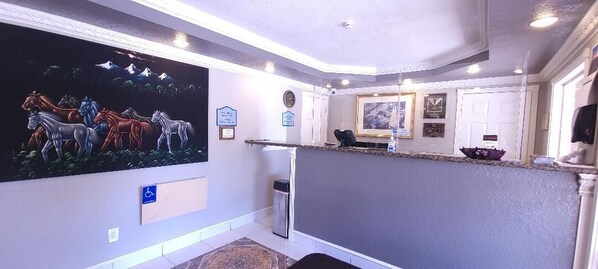 A reception area with a large wall mural, a reception desk, a wheelchair-accessible sign, and a clock on the wall.