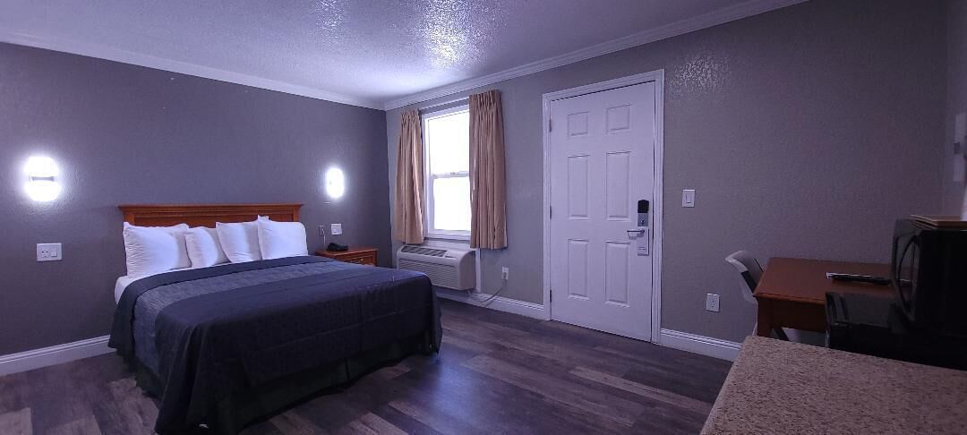 A hotel room with a bed, a desk, a chair, a window with curtains, and a door.