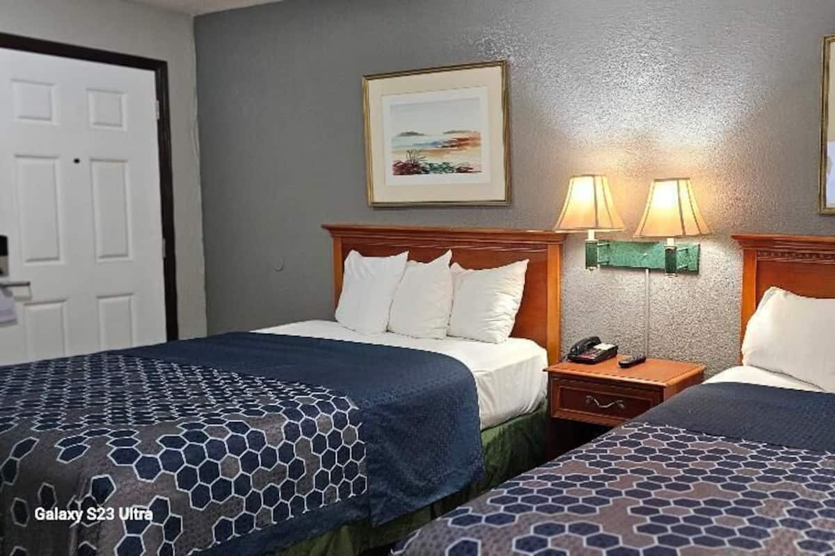 Habitación de hotel con dos camas, cada una con colcha estampada, cabecero de madera y mesita de noche con lámpara.