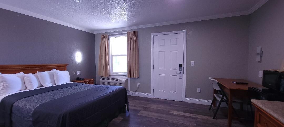 Une chambre d’hôtel avec un lit, un bureau, une chaise, une télévision et une porte.