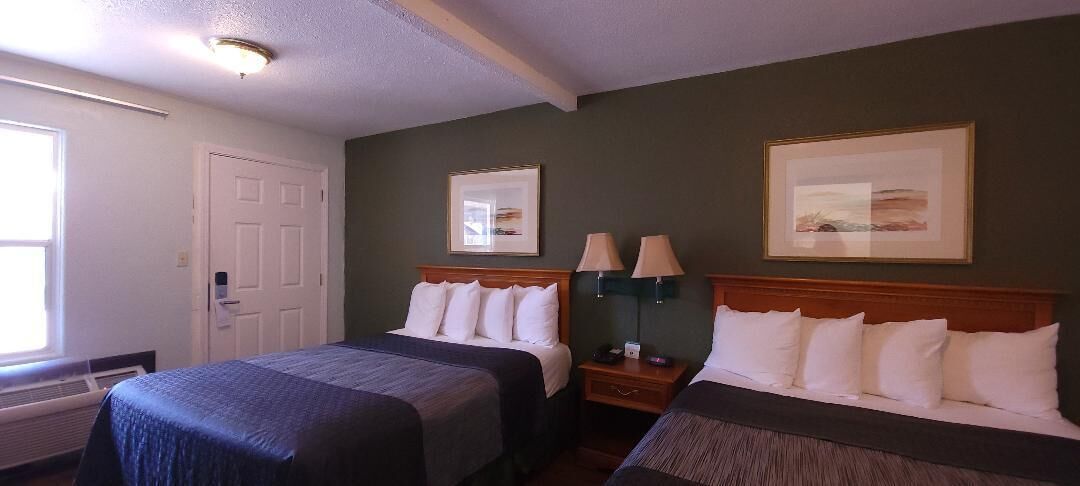A hotel room with two beds, a door, a window, and two wall-mounted lamps.