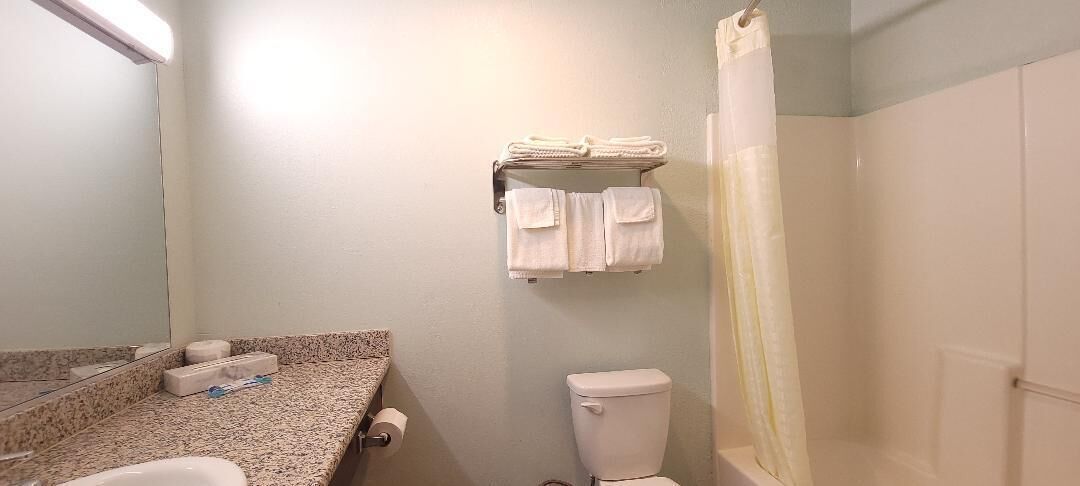 Un baño con encimera de granito, un inodoro, un perchero con toallas dobladas y una cortina de ducha.