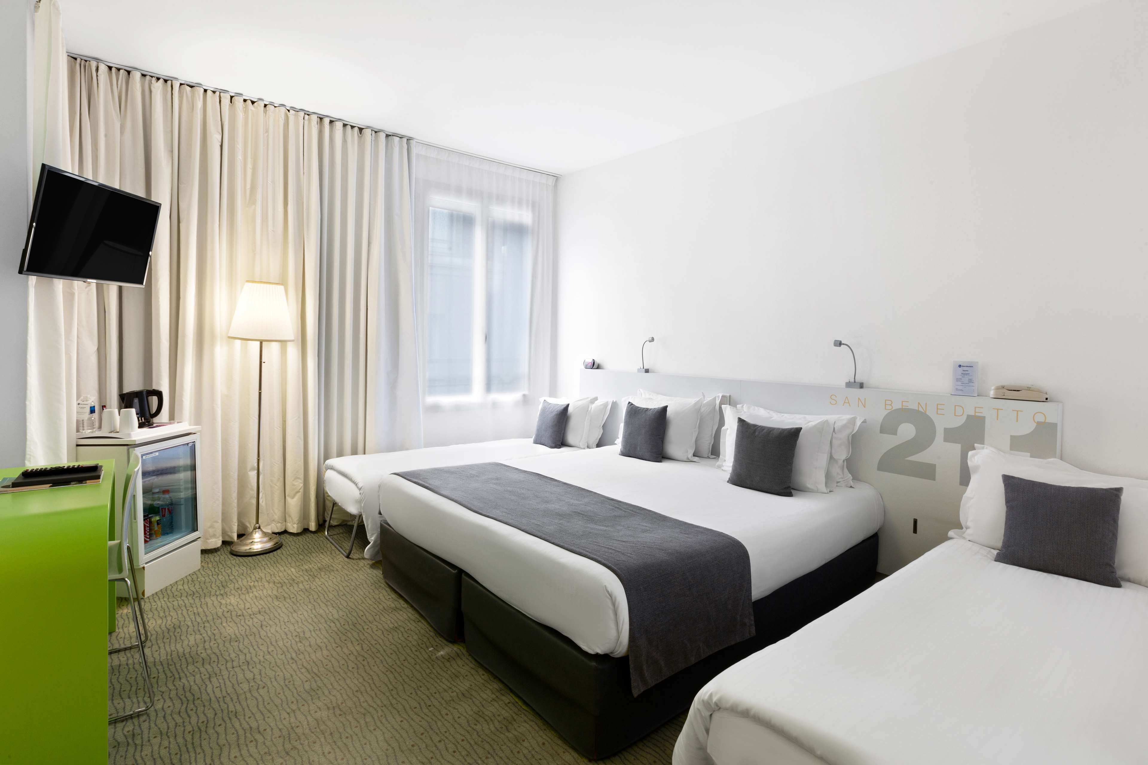 A hotel room with two beds, a TV, a desk with a lamp, and a view of the city.