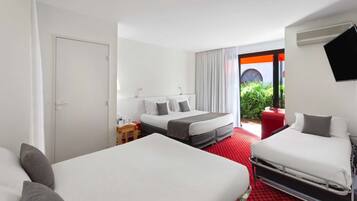 A hotel room with two beds, a red carpet, a TV, a window with curtains, and a view of greenery outside.