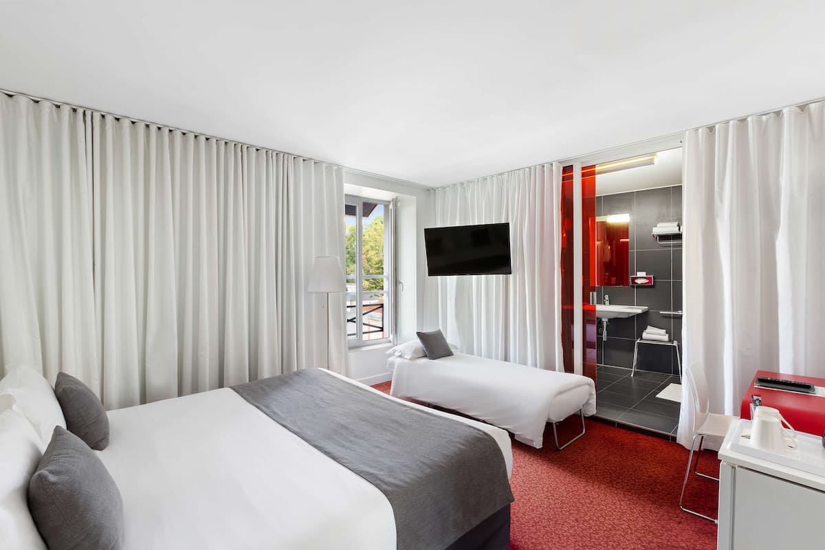 A hotel room with two beds, a TV, a bathroom with a shower, and a red carpet.