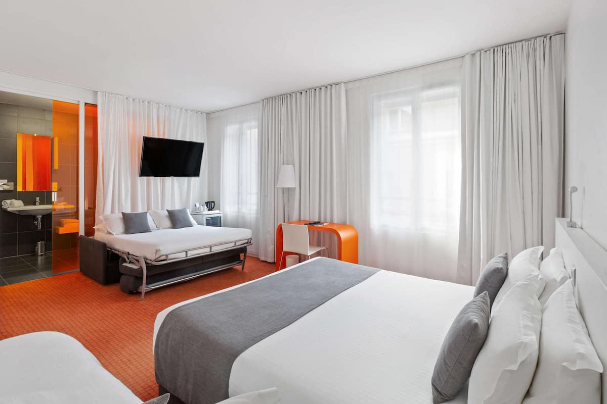 A hotel room with a large bed, a desk, a TV, and a bathroom with a mirror and sink.