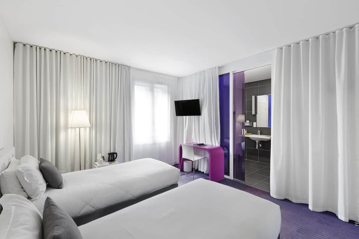 A hotel room with two beds, a desk, a TV, and a bathroom visible through an open door.