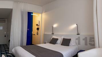 Habitación de hotel con cama, escritorio, silla, baño con ducha y puerta con marco azul.