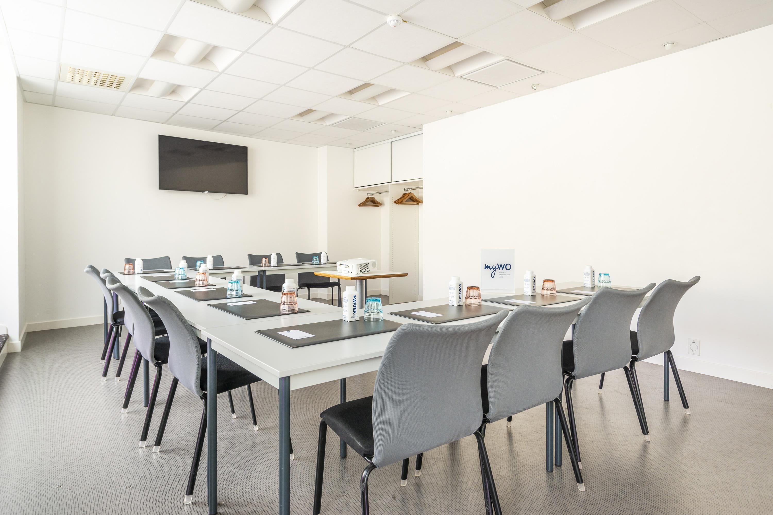 Une salle de conférence avec une longue table, de nombreuses chaises, un téléviseur à écran plat et un panneau indiquant « myWO ».