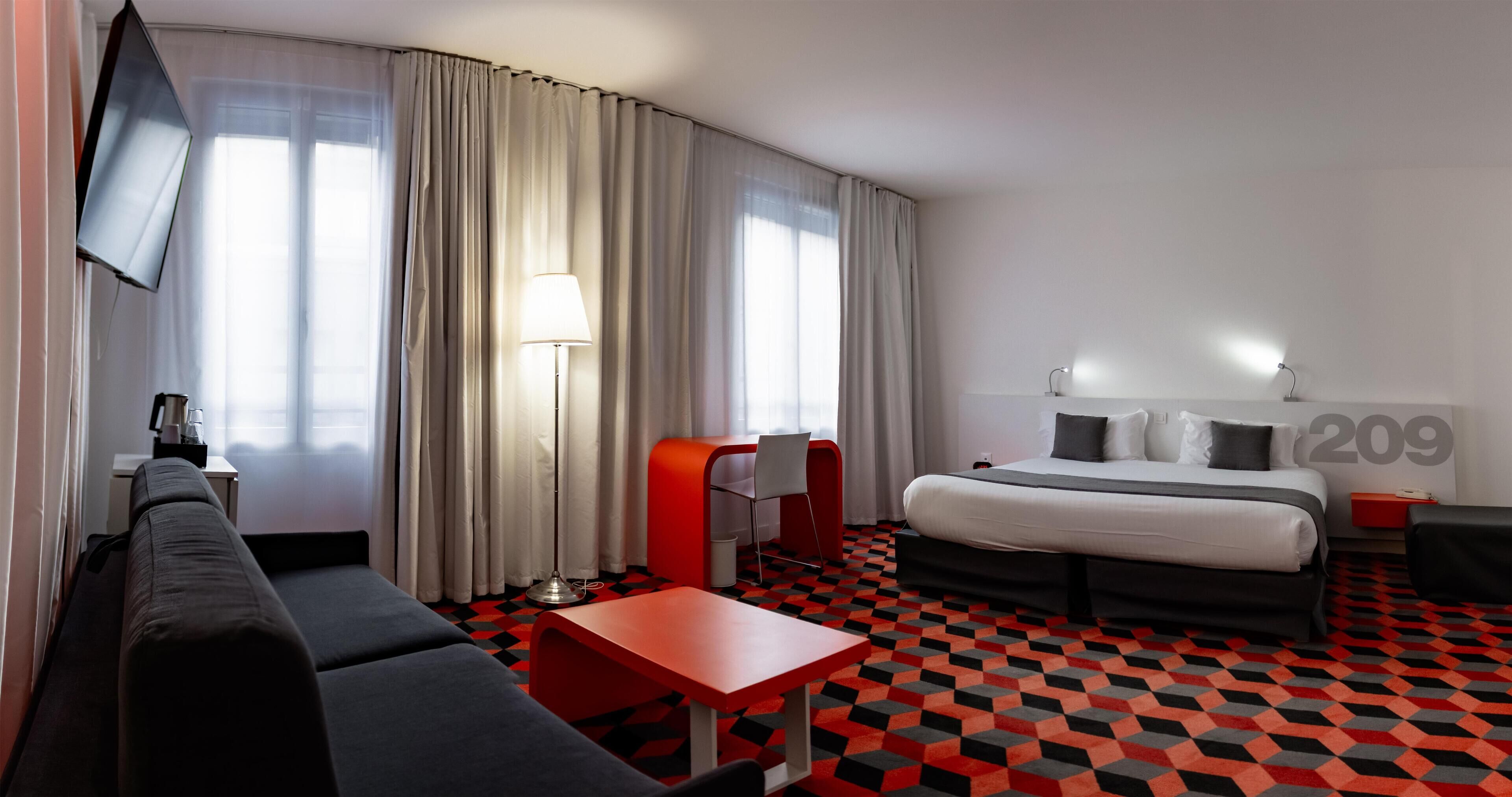 A modern hotel room with a curved bed, a red armchair, a small table, and a TV mounted on the wall.