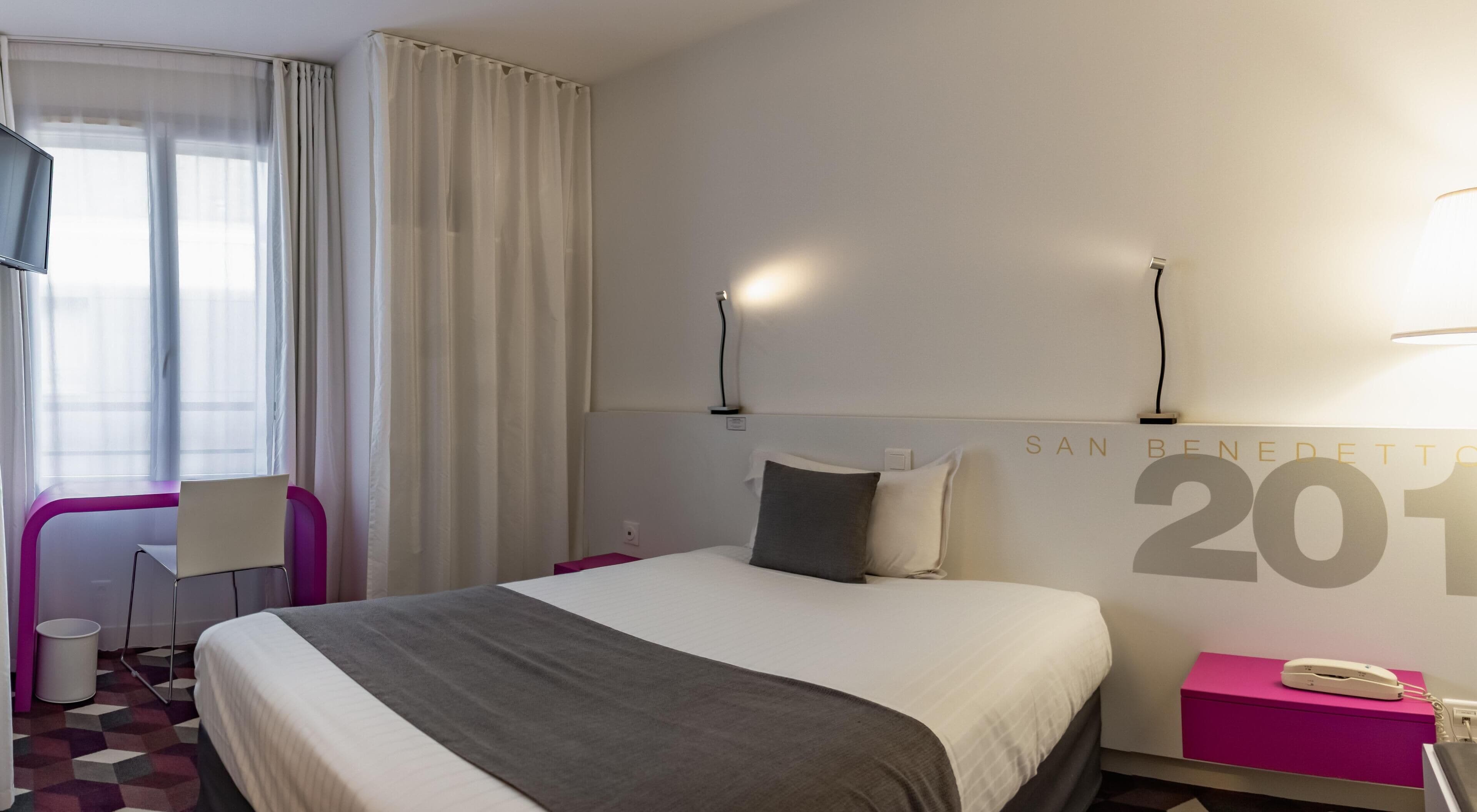 Ein Hotelzimmer mit einem Bett, einem Sessel, einem Schreibtisch, einer Lampe und einer Wand mit dem Jahr 2017.
